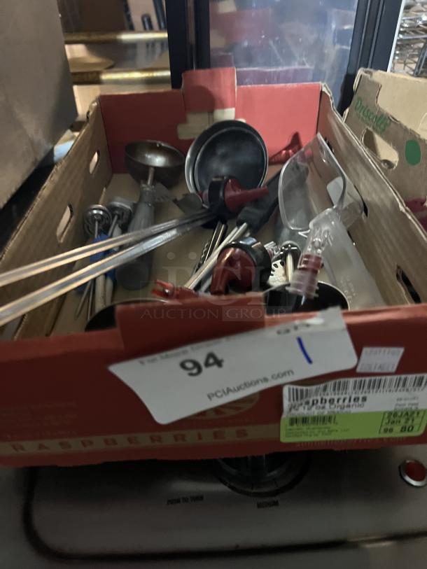 Box of assorted kitchen utensils in varying condition, including ladles, tongs, and measuring spoons. Auction label visible.