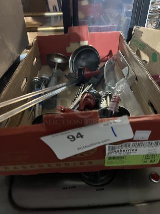 Box of assorted kitchen utensils in varying condition, including ladles, tongs, and measuring spoons. Auction label visible.