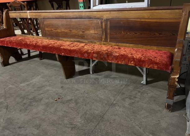 Antique church pew with crushed red velvet seat, ornate woodwork, and signs of wear.Suitable for restoration or decor.