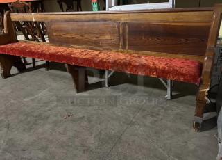 Antique church pew with crushed red velvet seat, ornate woodwork, and signs of wear.Suitable for restoration or decor.