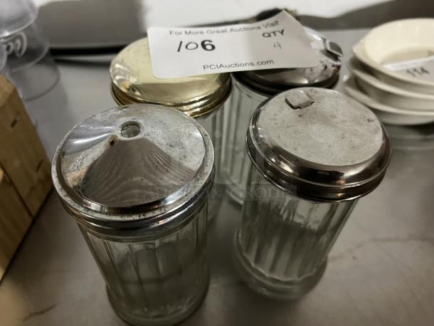 Set of four vintage glass sugar/creamer shakers with metal lids, slightly worn. Auction tag shows item number 106 and quantity 4.