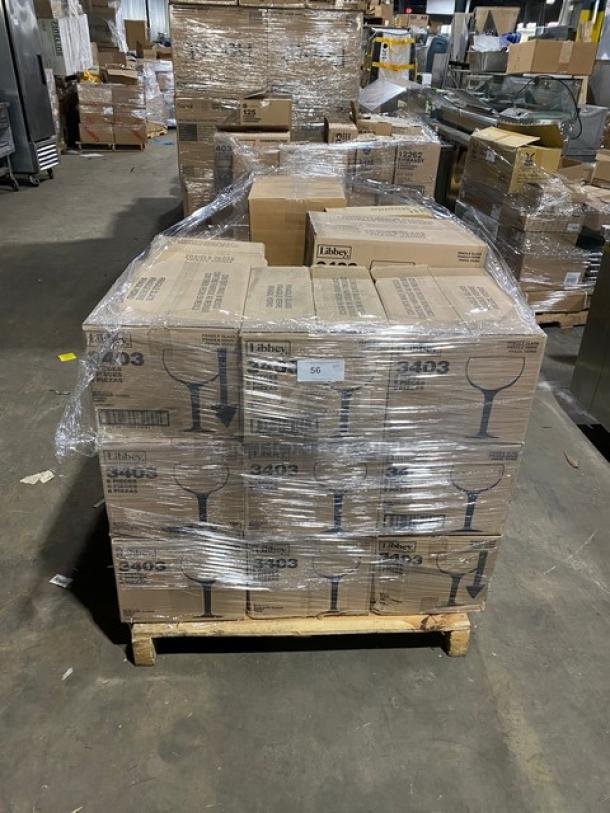 Mixed pallet of brand new Libbey glassware, including 38 oz. Super Bowl Glasses (Model 3403), wine goblets, mini martini glasses, and TableCraft cruet sets, wrapped and stacked on a wooden pallet in a warehouse.
