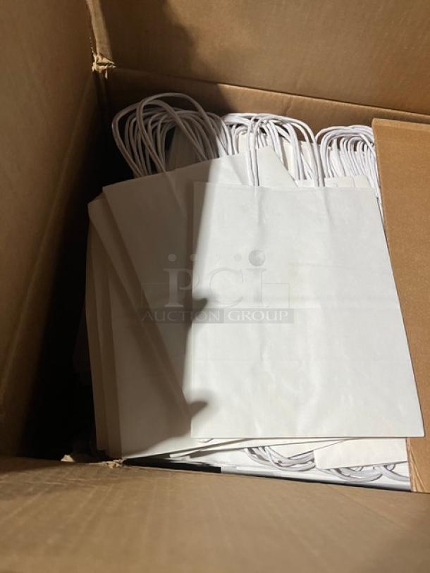 Cardboard box containing white paper bags with handles, new condition, stacked neatly.