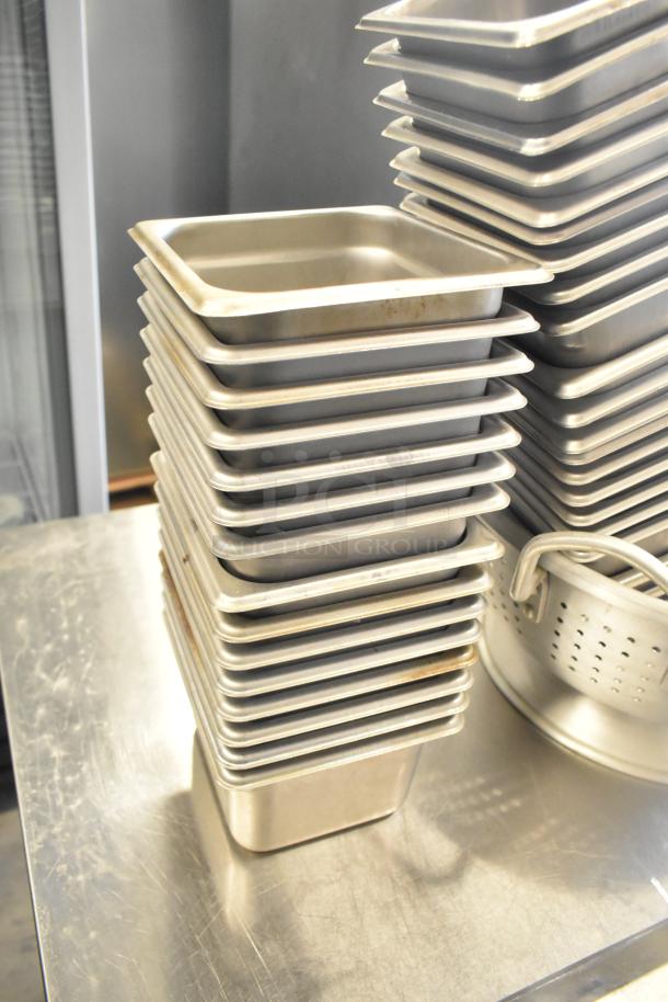 Stack of stainless steel drop-in bins and a colander on a table, part of a 47-item lot auction. Items in used condition.