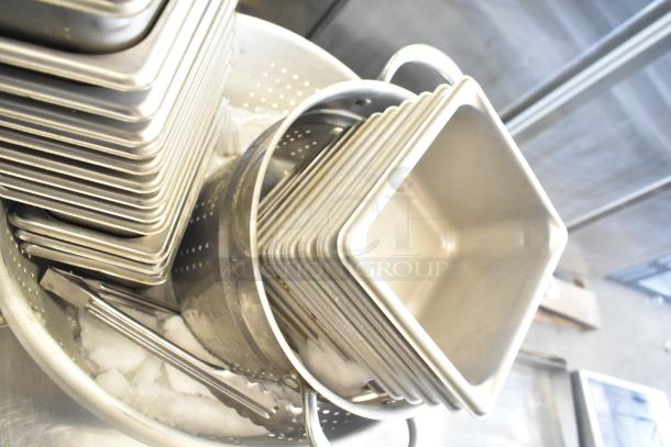 47 stainless steel items, including drop-in bins and a colander, stacked with tongs. Good condition, ideal for kitchen use.