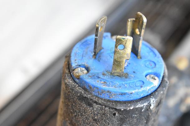 Close-up of a worn, blue electrical connector with visible grime and metal prongs.