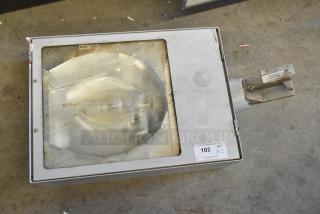 Industrial light fixture in metal casing with glass cover, visible rust and wear. Auction tag notes item 103, quantity 2.