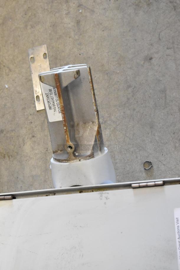 Industrial light fixture with metal bracket, slight rust, "IMPORTANT THIS BRACKET TO BE MOUNTED TO LUMINAIRE" label.