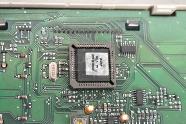 Close-up of a green circuit board with visible chip labeled "BOSCH © 2005" and various electronic components and connections.