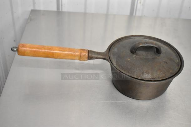 Vintage metal pan with a wooden handle and lid, showing signs of wear, suitable for display or collection.
