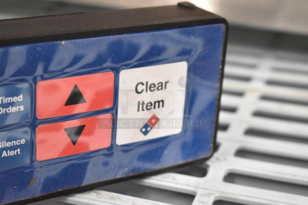 Blue control panel with buttons labeled "Timed Orders," "Silence Alert," and "Clear Item." Features directional arrows and a logo.
