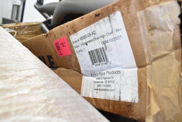 Brown cardboard box with Koala Kare high chair. Label shows model KB950-09-KD, unassembled, quantity 1, and manufacturer details.