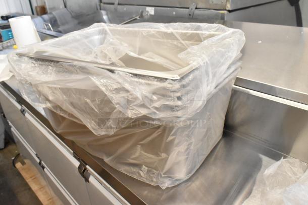 Plastic-wrapped stack of new scratch and dent food service items including Vollrath and Choice stainless steel pans and a bus tub.