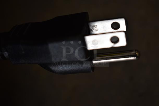 Close-up of a power plug, showing a black body with two metal prongs and a grounding pin, suitable for 120V appliances.