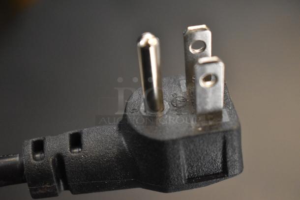 Close-up of a black power plug with three metal prongs, used for electrical appliances.