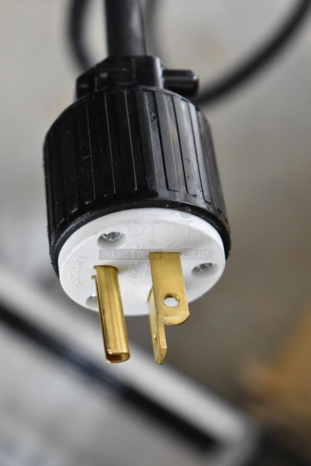 Close-up of a power plug for the ServIt 423HDM26SA heated display case. Black housing, brass prongs visible.