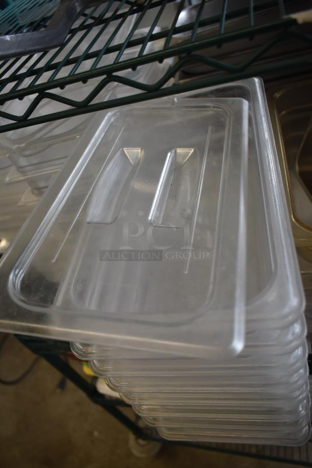 Stack of transparent polycarbonate drop-in bin lids, new, on a metal rack, part of a mixed item auction lot.