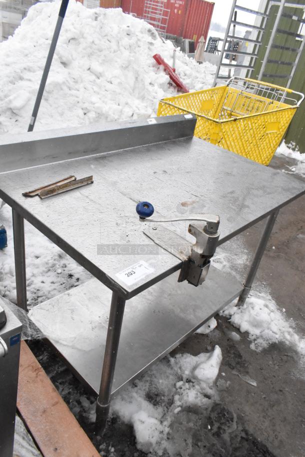 Metal table with commercial can opener, features under shelf and durable stainless steel construction. Some visible wear.
