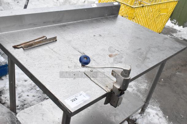 Stainless steel table with commercial can opener, under-shelf, and visible wear; ideal for industrial use. Tag reads "203".