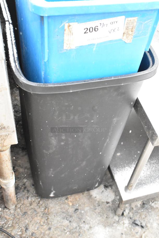 Two poly trash cans, blue and black, with scuffs and dirt. Label on blue can reads "206/QTY VX2", showing signs of wear.