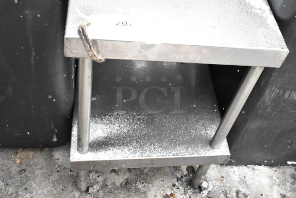Commercial equipment stand with under shelf, stainless steel, showing signs of outdoor use with light snow and wear.