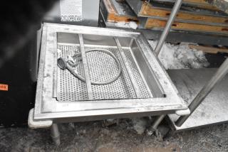 Stainless steel bin with straining insert on commercial casters, snowy surface, includes coiled hose, durable for heavy use.