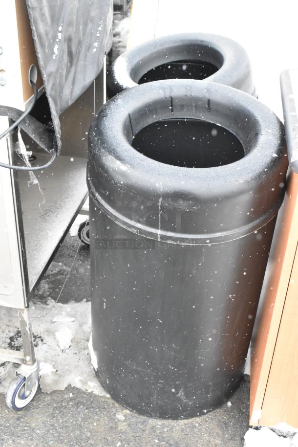 Three trash can shells, including two black cylindrical plastic and one wooden. Outdoor setting, lightly snow-dusted. Durable and functional.