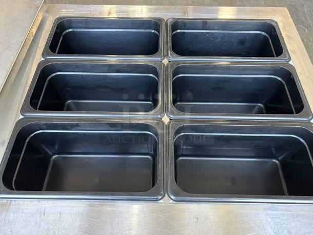 Continental Refrigerator SW60-24M prep table with six black food pans, stainless steel surface, in exceptional condition.