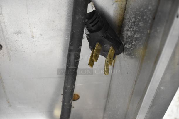 Close-up of a 208 Volt, 3-phase electric plug connected to a commercial appliance, showing prongs and black cord.