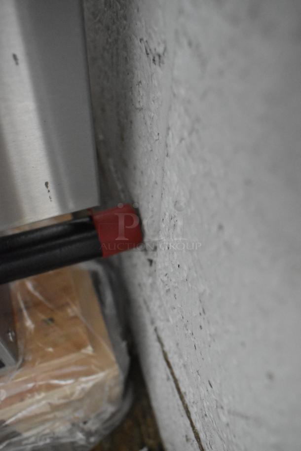This image shows a close-up of the side of a commercial griddle near a wall. The visible section includes a red-capped component.