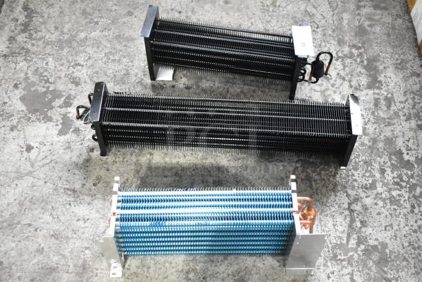 Three brand new scratch and dent evaporator coils with visible fins and copper tubing on the floor.