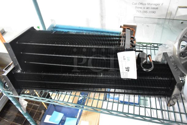Brand new scratch and dent evaporator coils, black metal fins, auction tag indicates quantity of 3, on metal shelf.