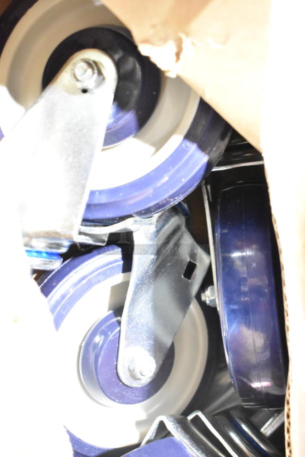 Box of brand new commercial casters, blue wheels, slight scratches, dented box visible, metal brackets intact.