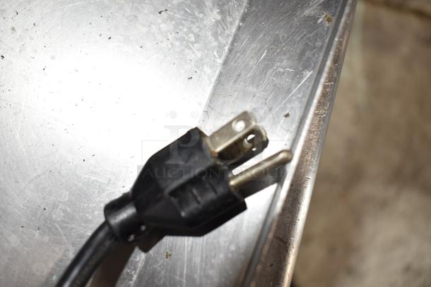Black power cord plug on metallic surface, photographed close-up.