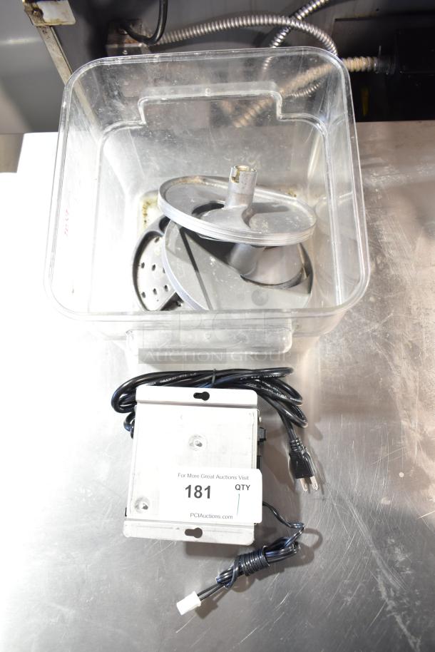 Clear poly bin with 3 food processor blades and a Lancer power supply, good condition. Auction tag #181 visible.