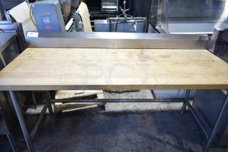 Butcher block table with wooden top and metal frame; surface shows signs of use, highlighting durability.