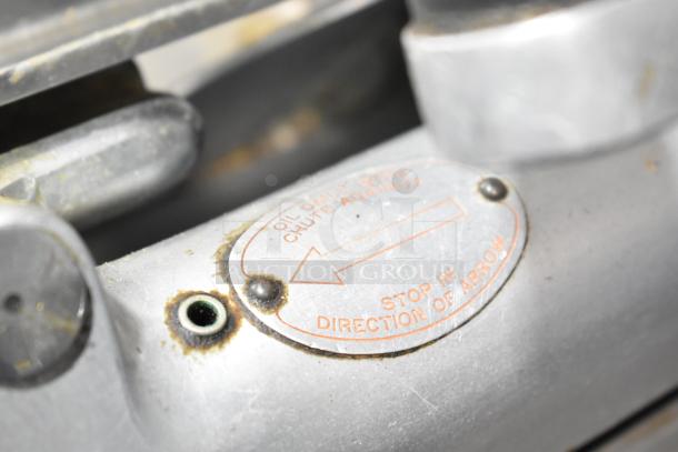 Globe Commercial Automatic Meat Slicer, visible wear, with blade sharpener. Tag reads: "Oil daily with chute against, stop in direction of arrow."