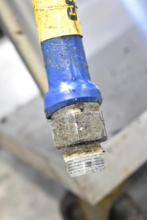 Close-up of a blue gas hose connection, part of a Vulcan countertop gas charbroiler grill. Visible wear and usage marks.