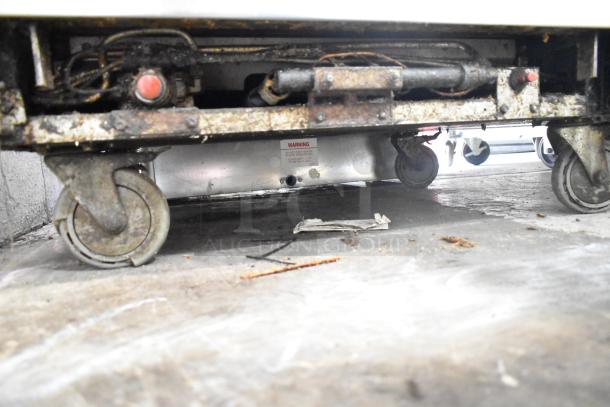 Bakers Pride gas range with 6 burners, flat top griddle, cheese melter, 2 ovens, and backsplash, on wheels; visible wear.