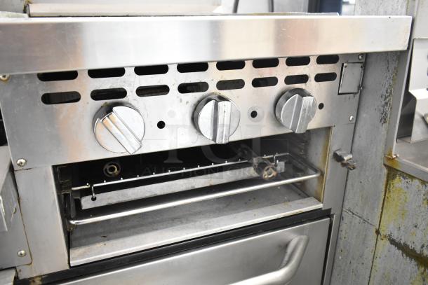 Bakers Pride commercial gas range with 6 burners, flat top griddle, cheese melter, 2 ovens, and back splash. Signs of use.