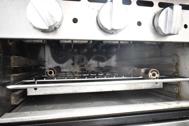 Bakers Pride commercial gas range with 6 burners, flat top griddle, cheese melter, 2 ovens, and backsplash. Used condition.