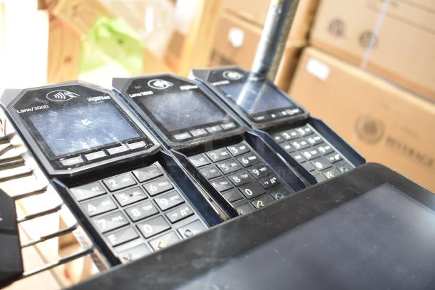 Three Ingenico Lane/3000 credit card readers, with visible wear, part of an auction lot including four POS monitors.