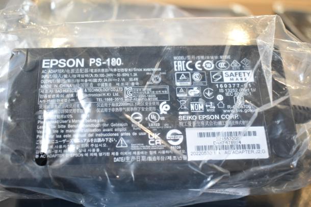 Epson PS-180 AC adapter with safety certifications and model details visible, wrapped in plastic packaging.