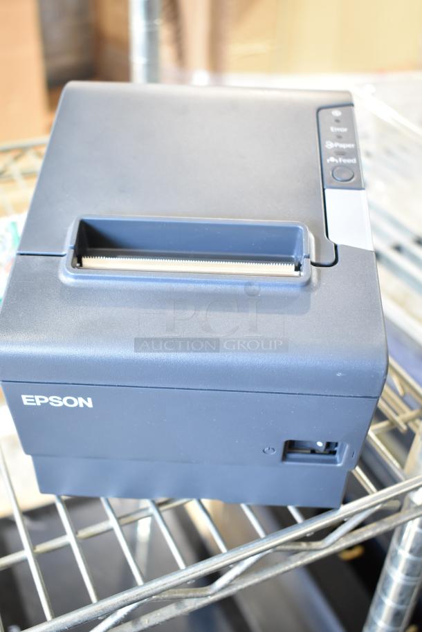 Epson M244A receipt printer, black, in used condition on metal shelf, with visible control buttons on top.
