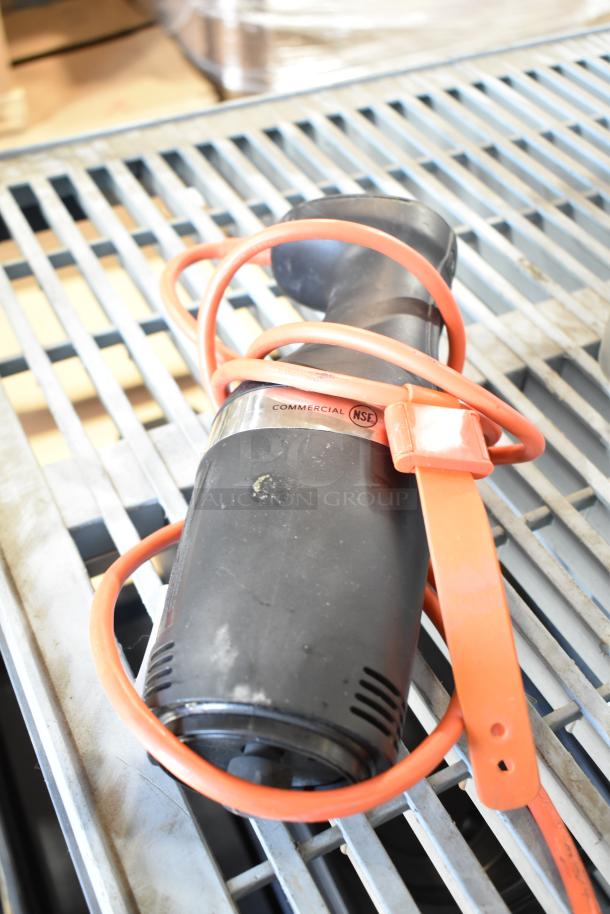 Black immersion blender, no blade, 115 volts, 1 phase, NSF certified, with orange cord, on metal grate.