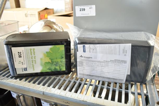 Two Georgia-Pacific countertop napkin dispensers, black, new condition with visible warranty papers, ideal for commercial use.