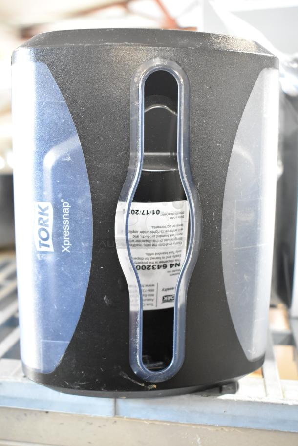 Tork Xpressnap countertop napkin dispenser, black and blue, front view, visible label with instructions.