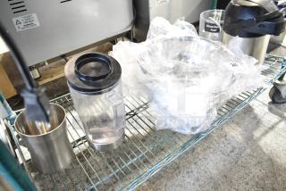 Various kitchen items including a blender pitcher, metal cup, and bowls on a shelf. Some items wrapped in plastic. Label indicates "Strawberry Acai."