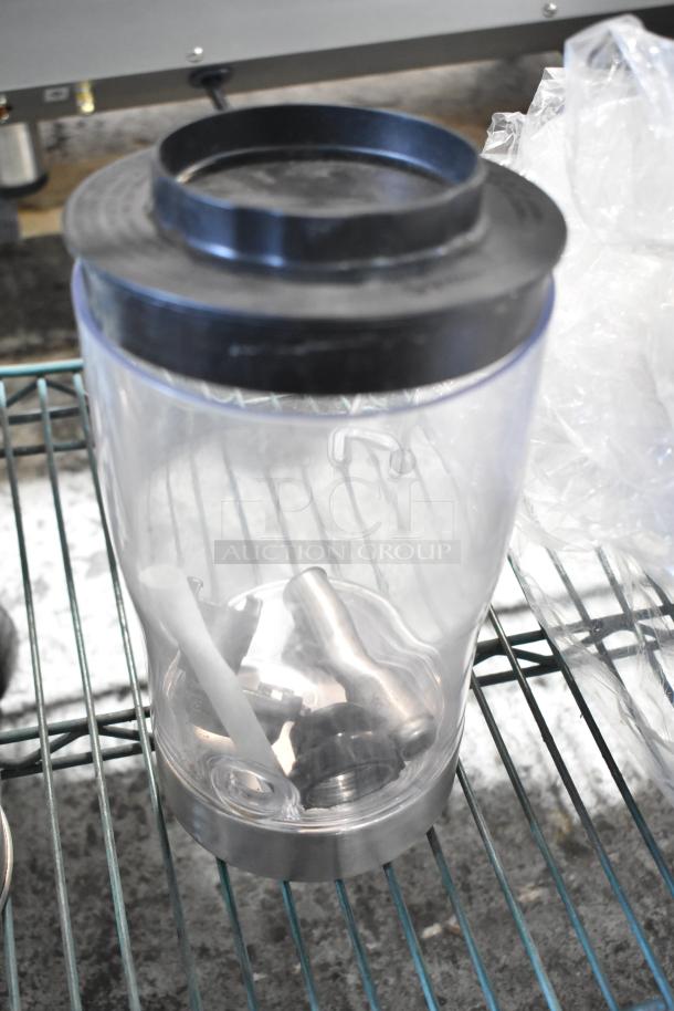 Blender pitcher with black lid on metal shelf, containing metal components; part of a tier lot of various items.