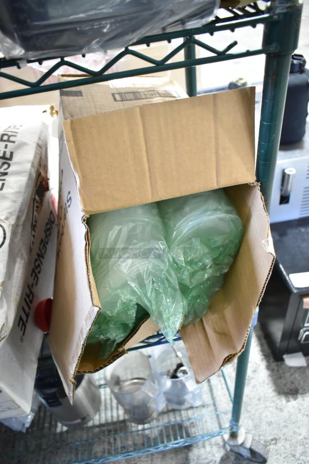 Six various cup dispensers with lids in open cardboard box; new condition, stored on metal shelf.